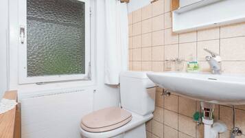 Ein Badezimmer mit Toilette, Waschbecken und einem Fenster mit Blick ins Freie.