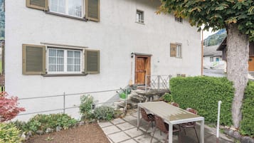 Un edificio blanco con balcón, una mesa con sillas y un pequeño jardín.