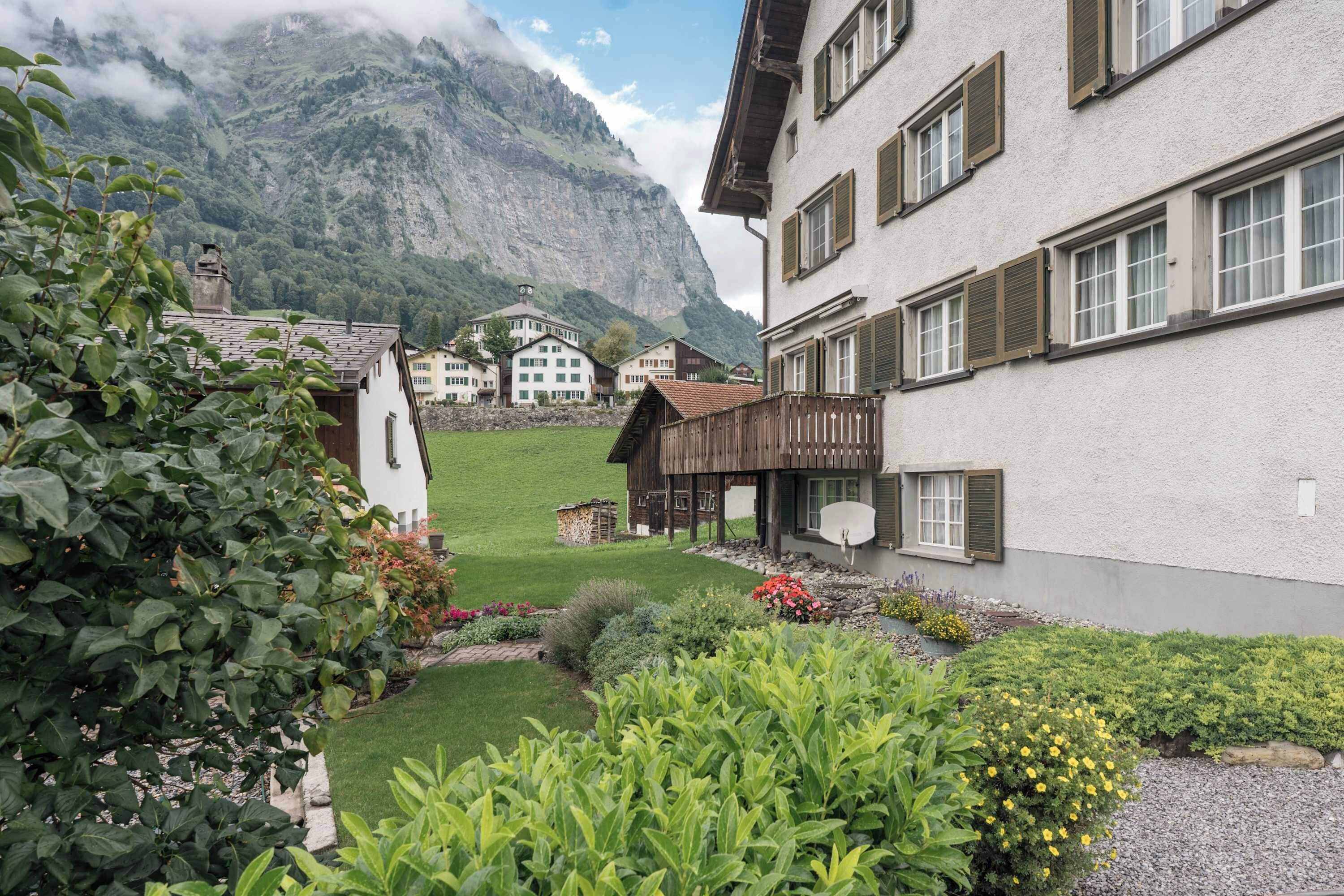 Un tradizionale chalet con le montagne sullo sfondo, un giardino curato e una vista chiara del paesaggio circostante.