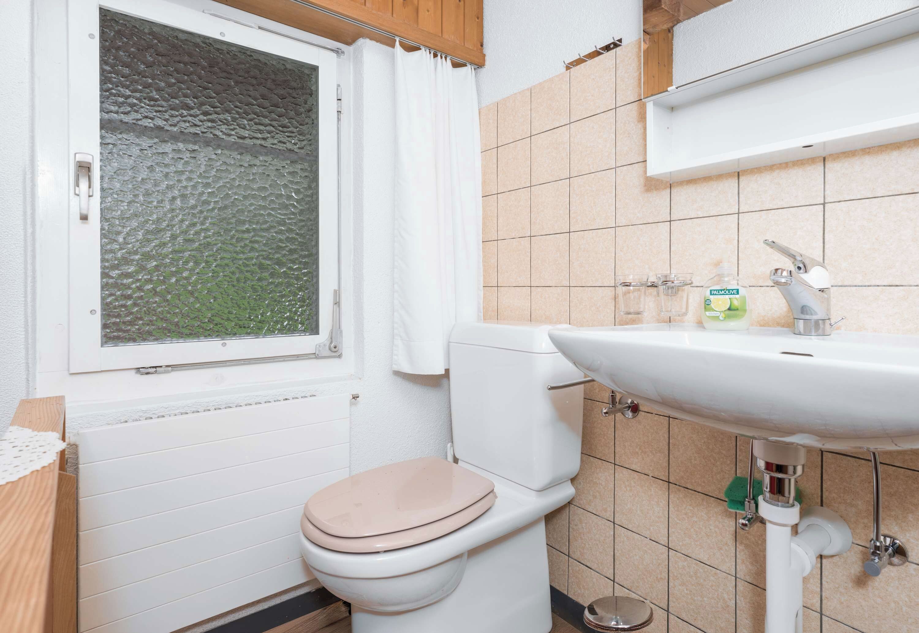 Une salle de bain avec des toilettes, un lavabo et une fenêtre donnant sur l’extérieur.