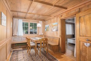 Un interior de madera con una mesa de comedor, sillas, un banco y vistas a través de una ventana.