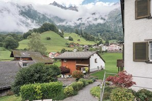 Un pueblo rural con casas, un jardín y montañas al fondo.