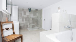 A modern bathroom with a bathtub, shower, and a glass-enclosed shower area. - Twin Room near Glarus, Desk & Parking (Glarus Süd)