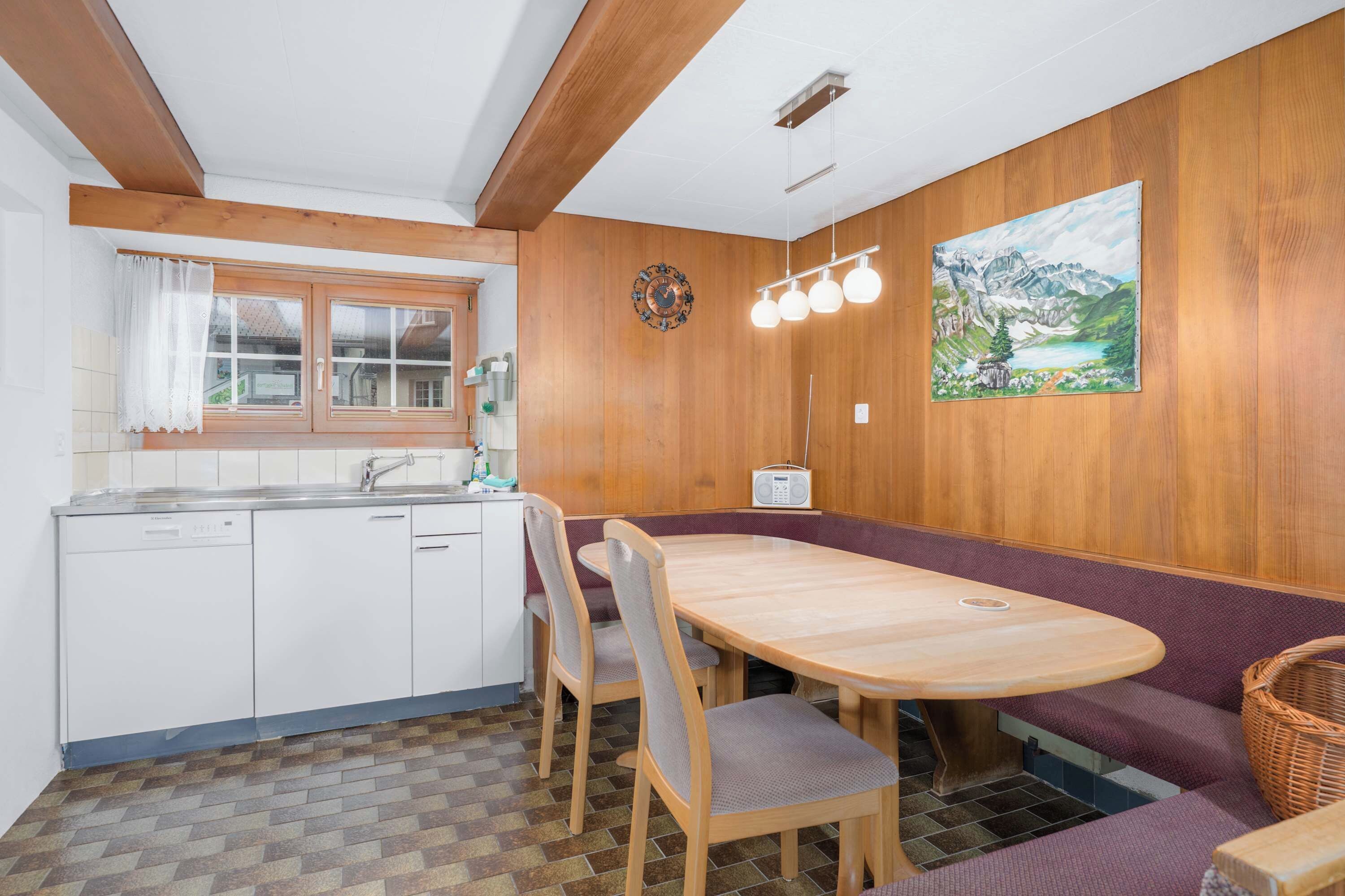 Una cucina compatta con una panca e un tavolo in legno, una radio e un quadro appeso al muro.