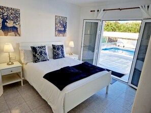 A bedroom with a bed, two bedside tables, a lamp, a large window, and a view of a swimming pool. - Villa Jude with private heated pool (Puerto del Carmen)