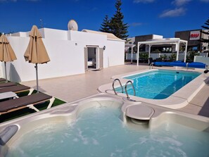 En pool på taket med solstolar och parasoller, ett bubbelbad och en byggnad med en skylt.