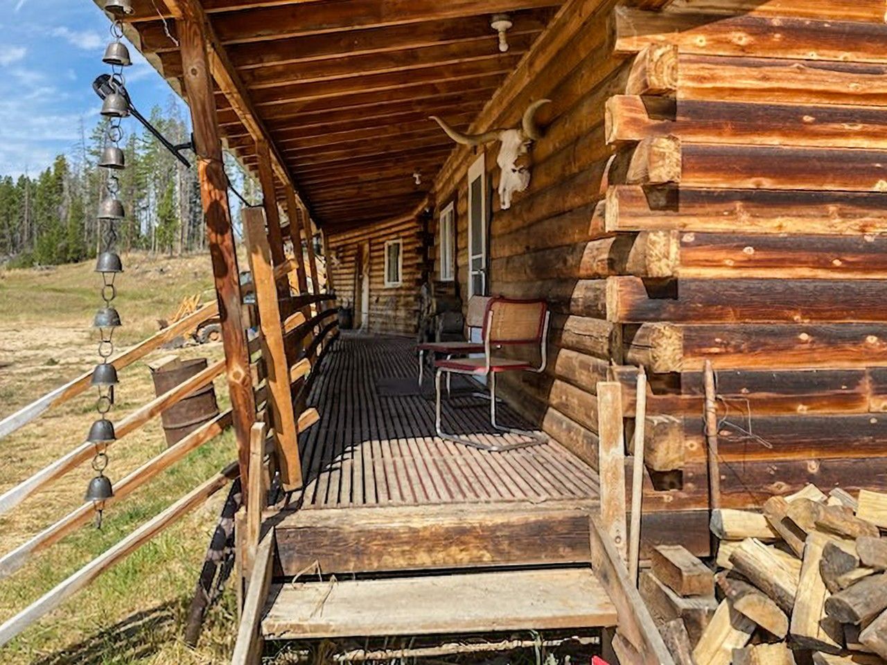 A log cabin with a porch, a metal bell, and a chair.