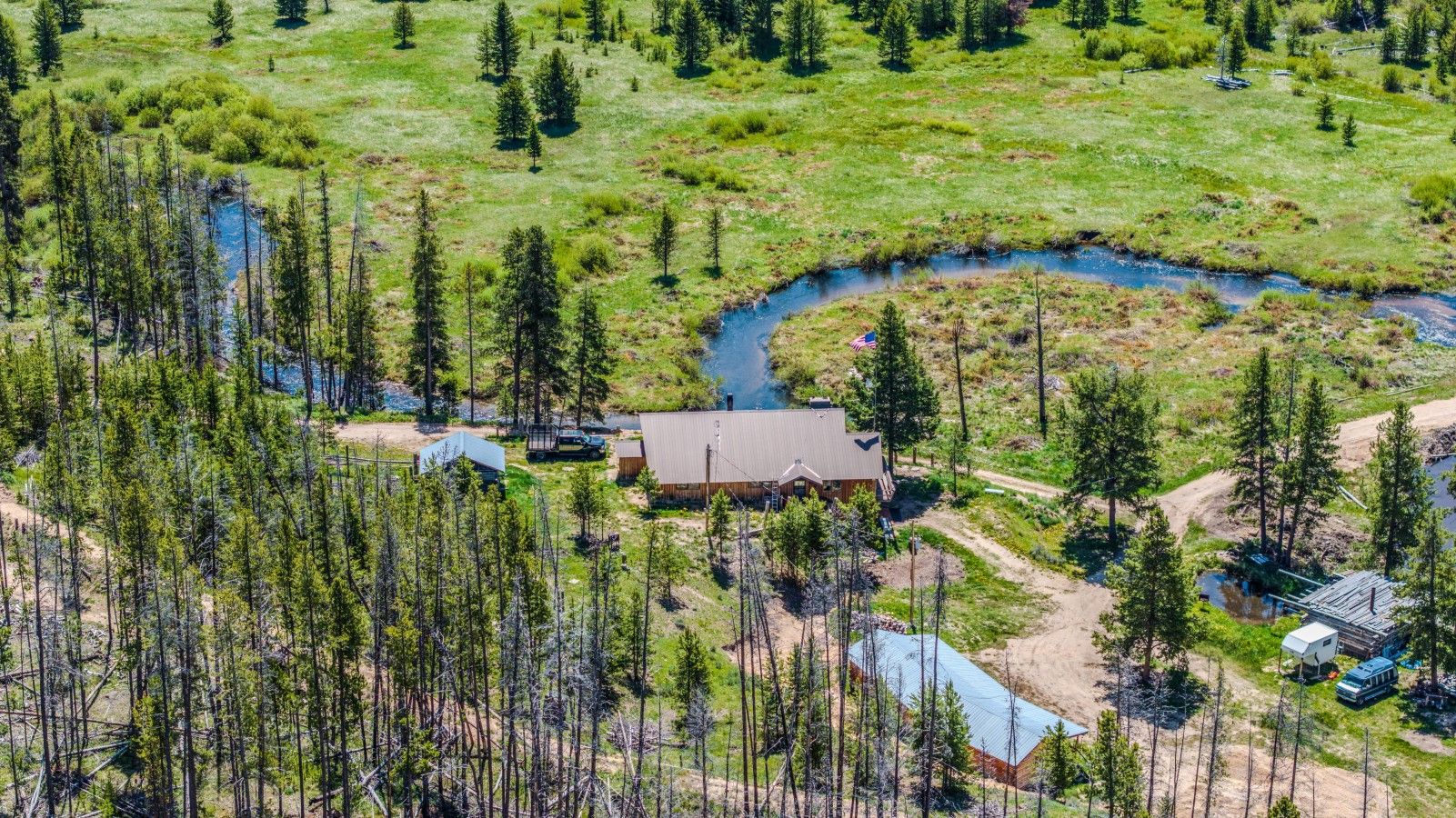 A remote cabin with a river nearby, surrounded by dense forest.