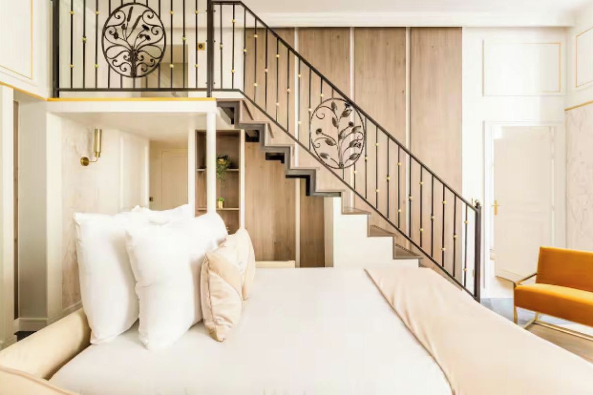 A bedroom with a bed, a staircase, and a chair.