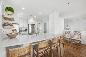 A modern kitchen with a large island, stainless steel appliances, and wicker chairs. - GULF-FRONT WATERCOLOR LUXURY CORNER UNIT, 2-STORY CONDO NEXT DOOR TO SEASIDE (Santa Rosa Beach)