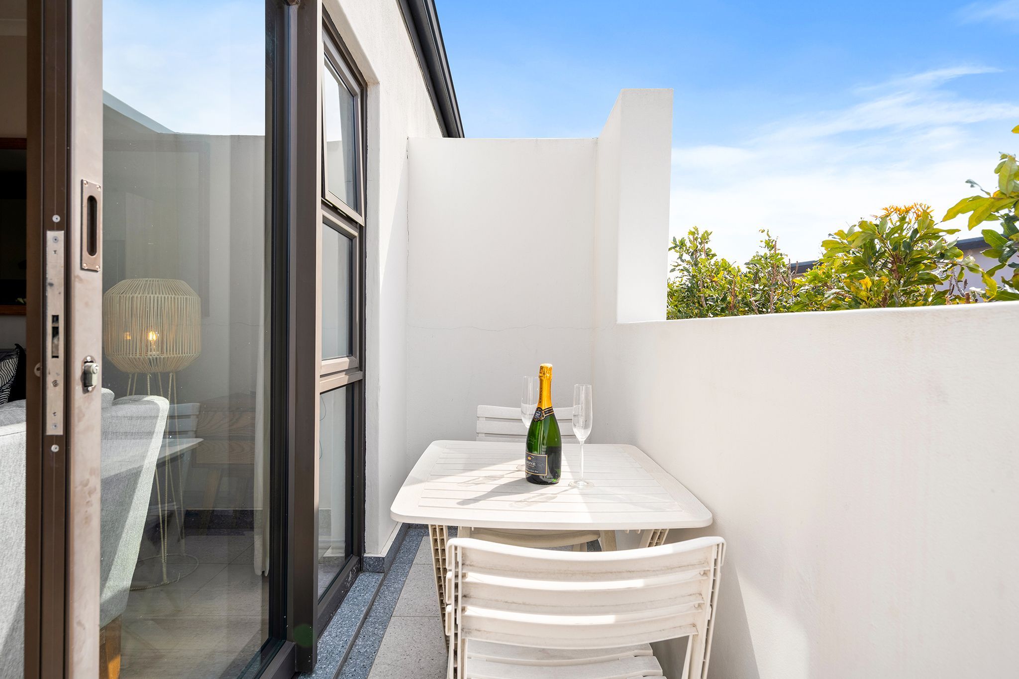 A small outdoor patio with a table and chairs, a bottle of champagne, and a glass.