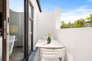 A small outdoor patio with a table and chairs, a bottle of champagne, and a glass. - Beachside Condo at Cape on Viola (Cape Town)