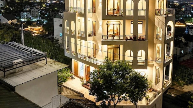Un hotel de varios pisos con balcones, amplias ventanas y vista al barrio circundante.