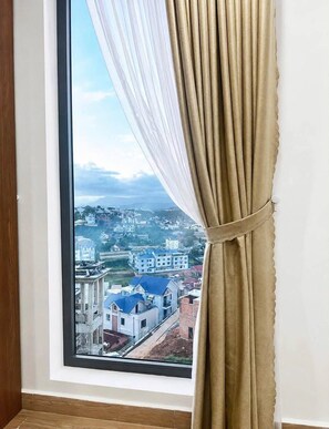 A window with a view of a residential area, curtains partially drawn, and a wooden floor.