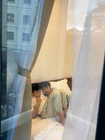 A room with a bed, a window with curtains, and a view of buildings outside.