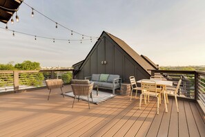 Eine Terrasse mit einer Couch, Stühlen und einem Tisch, umgeben von einem Geländer und Lichterketten.