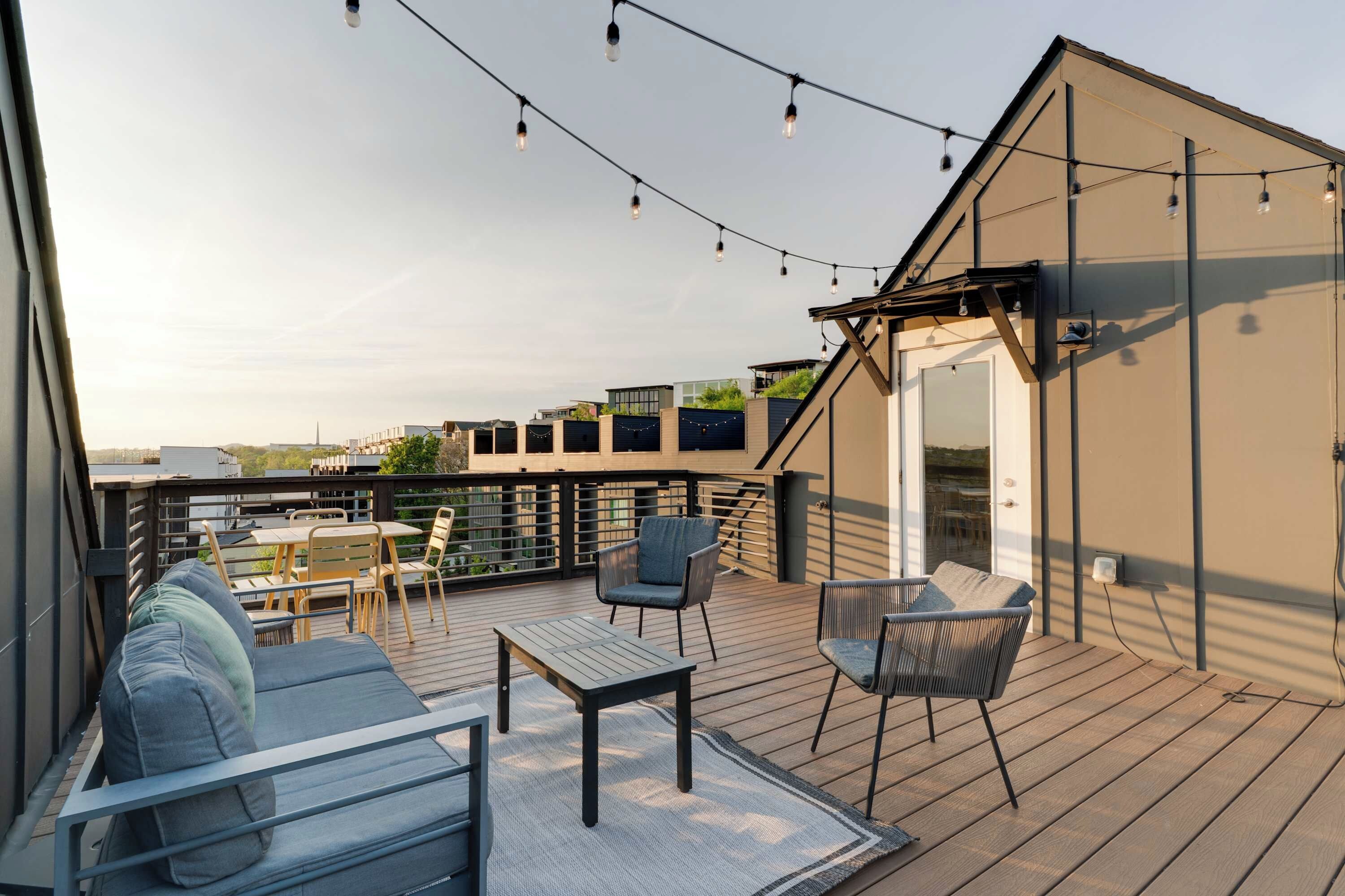 Een terras op het dak met een zithoek, lichtjes en uitzicht op de stadslijn.