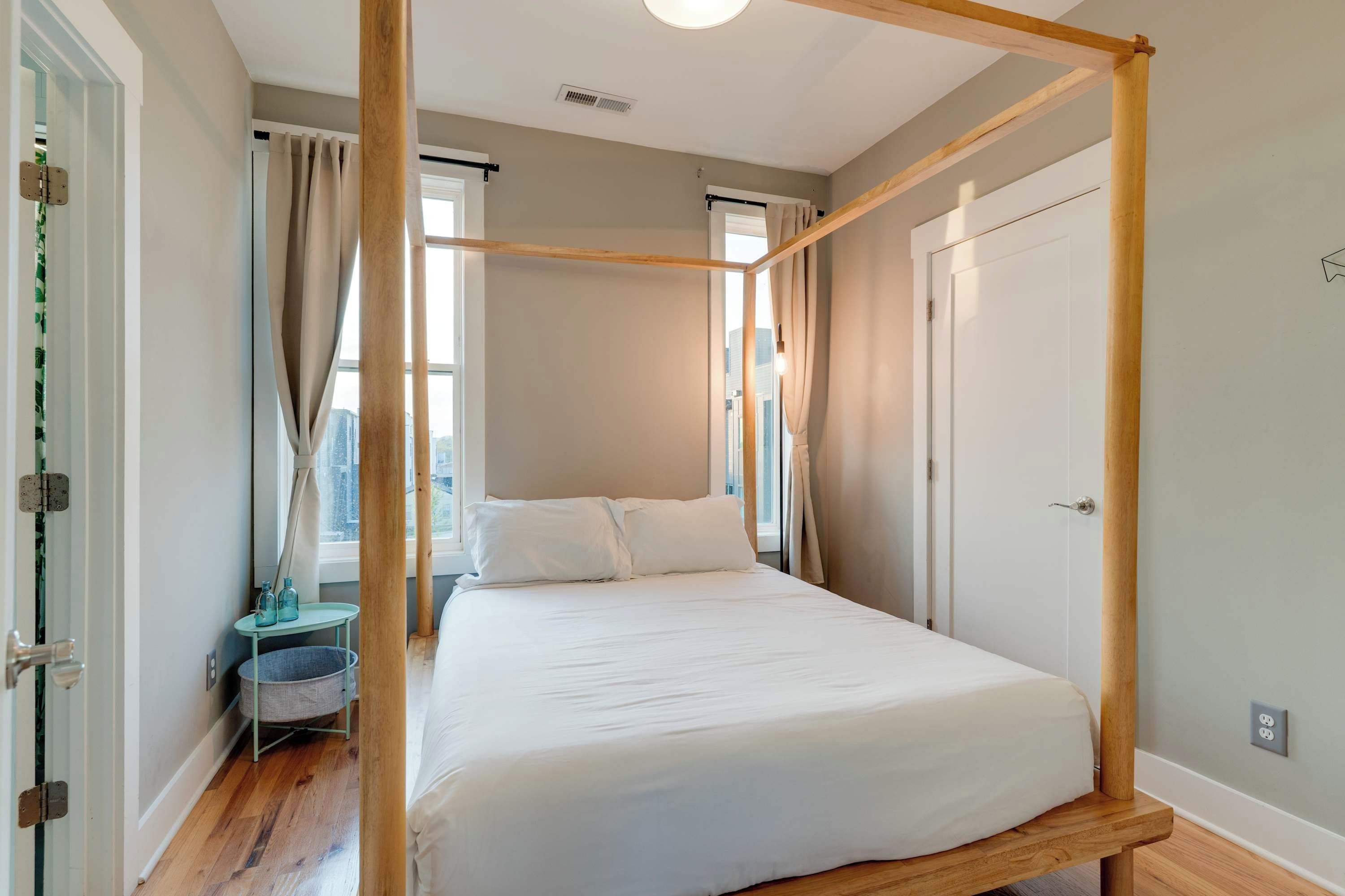 A bedroom with a four-poster bed, a small bedside table with a lamp, and a view of the city through the window.