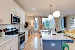 A modern kitchen with a central island, stainless steel appliances, and a dining area with a sofa and a green stool. - The Nashville Rooftop Retreat, Garage and Sleeps 8 (Nashville)