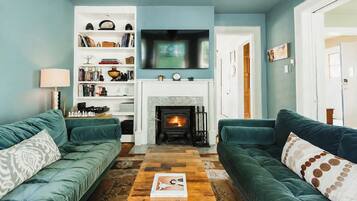 A living room with two green sofas, a fireplace, a bookshelf, and a flat-screen TV.