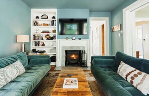 A living room with two green sofas, a fireplace, a bookshelf, and a flat-screen TV.