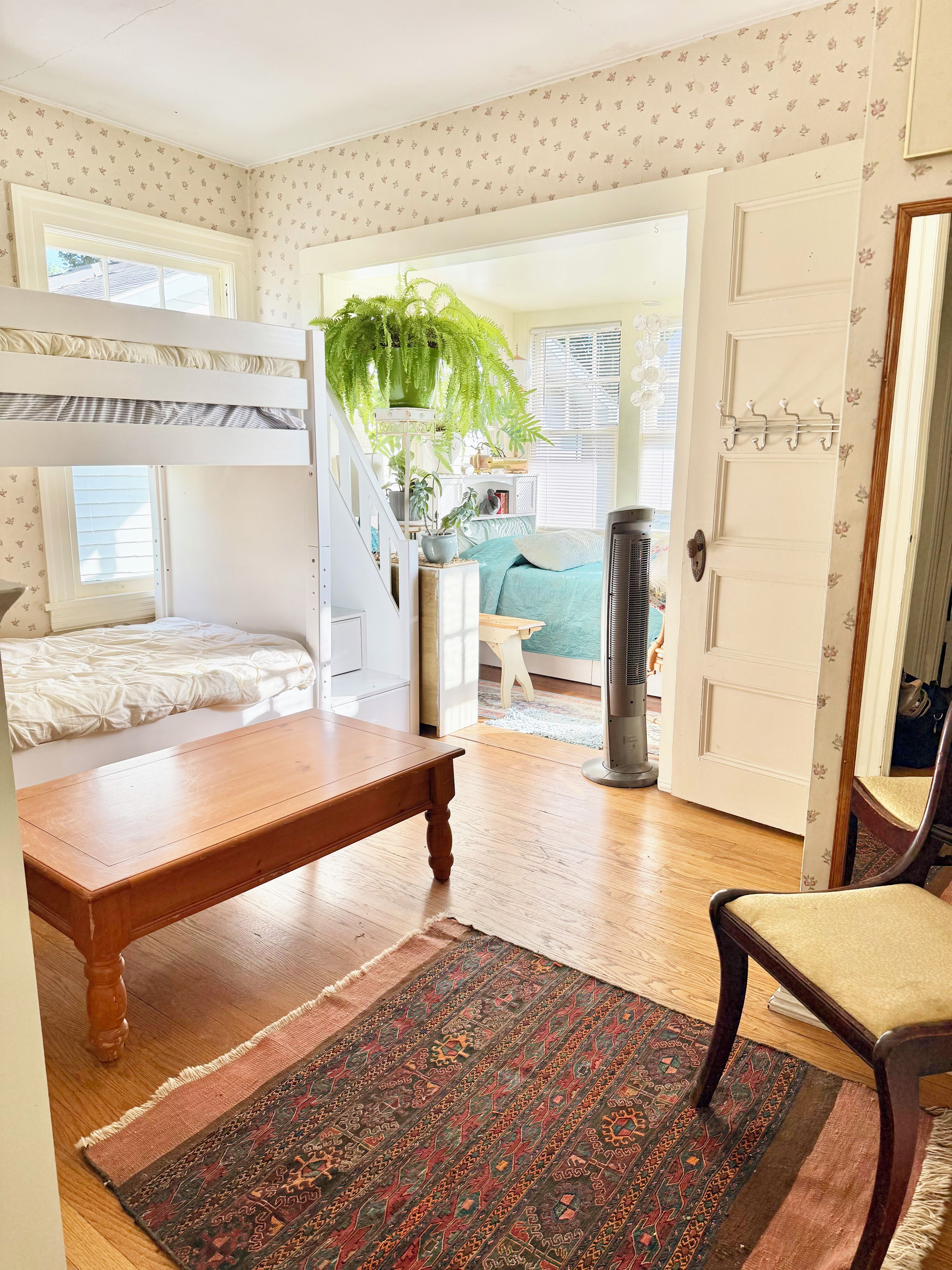 Una habitación con literas, una mesa de madera, una alfombra estampada y una silla.
