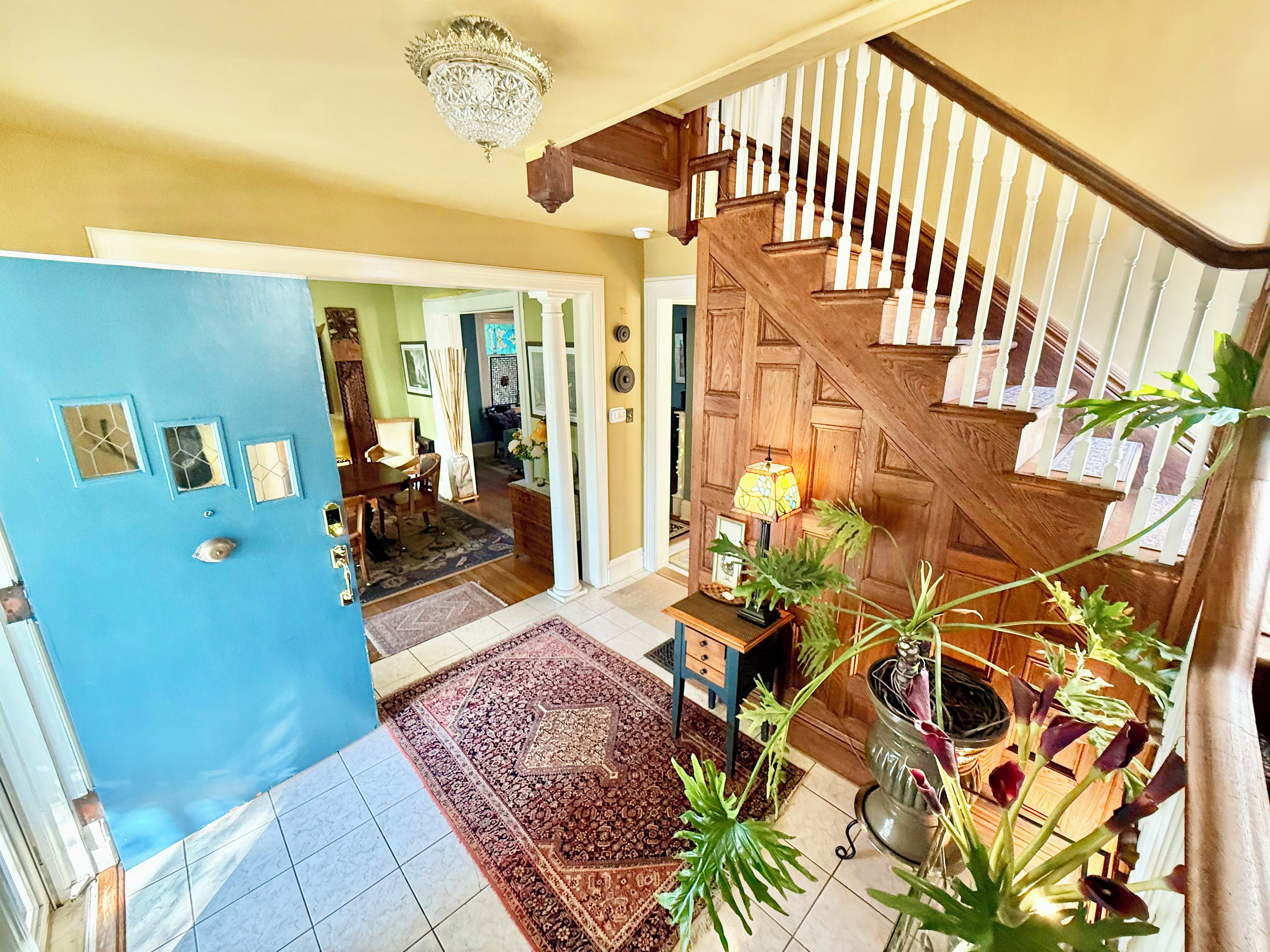 A spacious foyer with a wooden staircase, a chandelier, and a potted plant.
