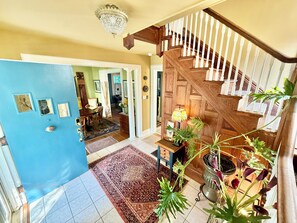 A spacious foyer with a wooden staircase, a chandelier, and a potted plant.