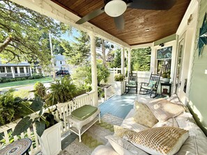 A covered porch with outdoor furniture, a view of the street, and a house in the background.