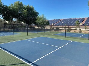 Ein Tennisplatz im Freien mit mehreren Spielfeldern, umgeben von einem Zaun, und Solaranlagen im Hintergrund.