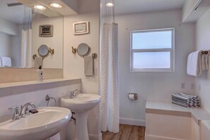 Ein Badezimmer mit zwei Waschbecken, einem Spiegel, einer Uhr und einem Fenster.