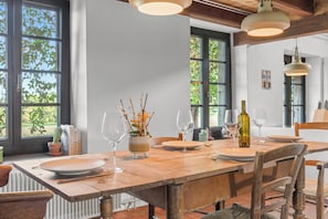 A dining area with a wooden table set for two, large windows, and a rustic ceiling.