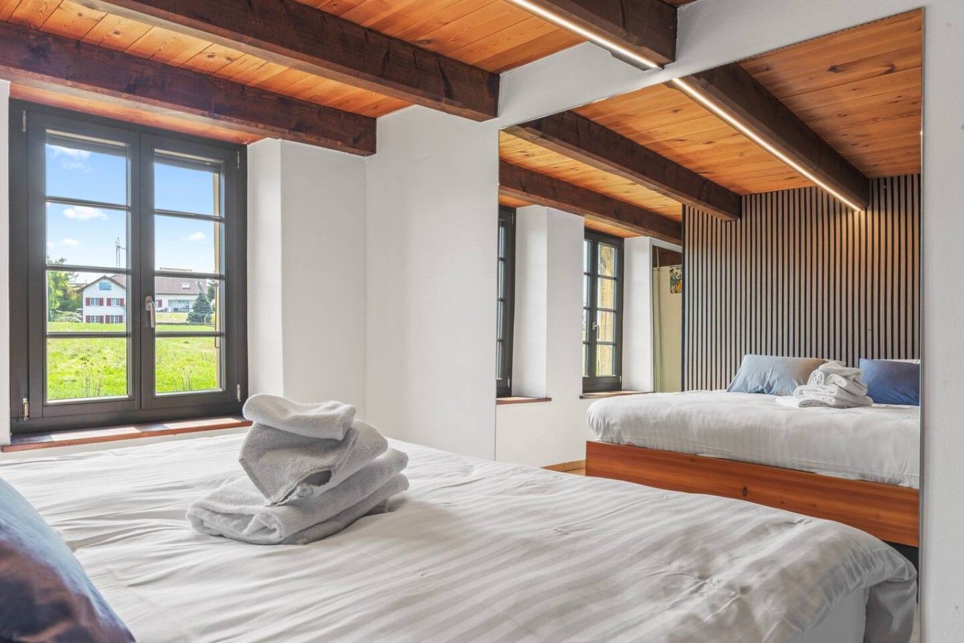 Une chambre avec deux lits, un plafond en bois et de grandes fenêtres.