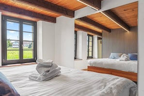 A bedroom with two beds, a wooden ceiling, and large windows.