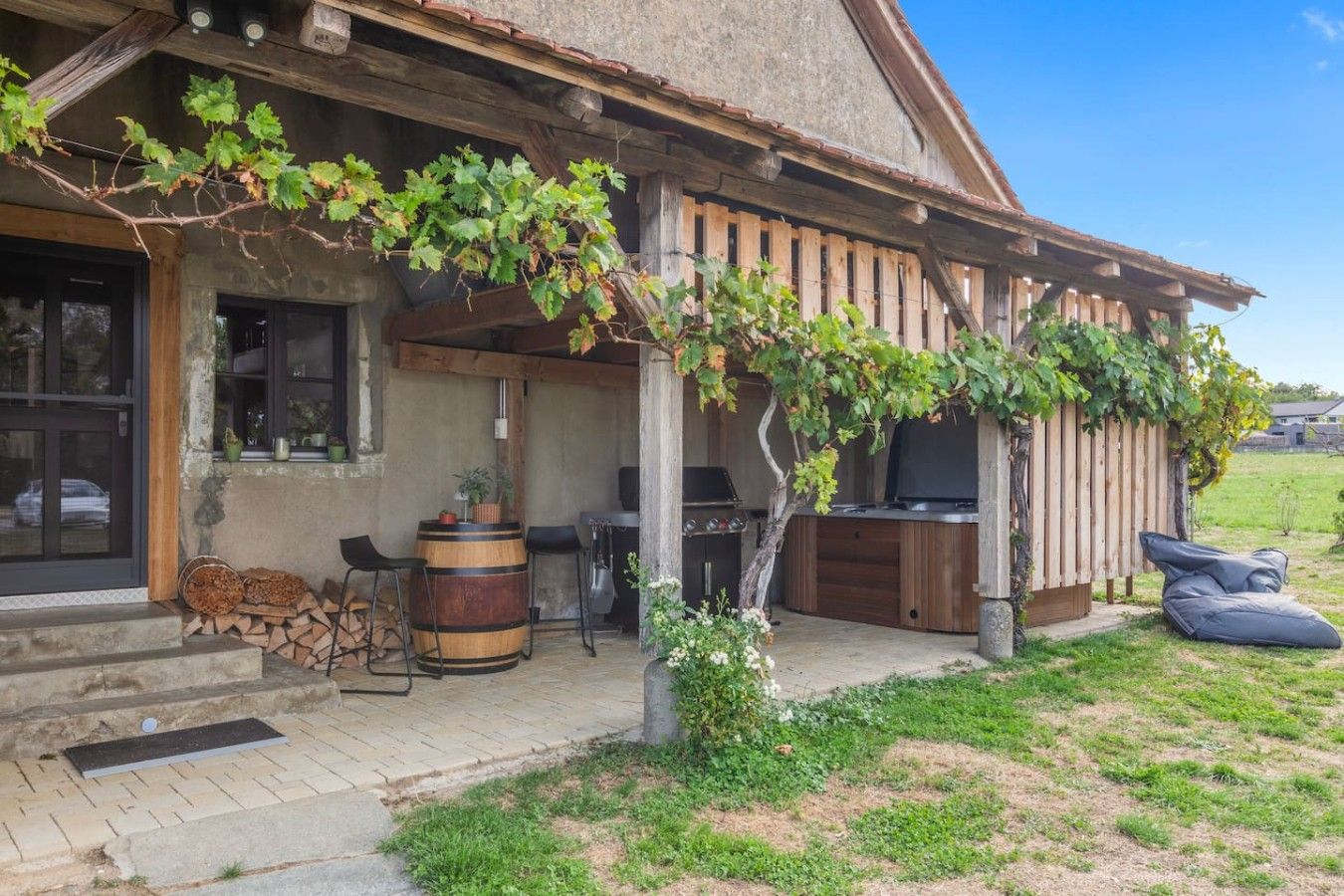 A rustic outdoor seating area with a wooden pergola, a barbecue grill, and a television.
