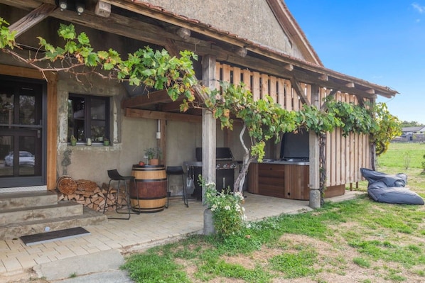 A rustic outdoor seating area with a wooden pergola, a barbecue grill, and a television.