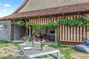 A patio with a table set for dining, a grill, and a wooden fence with vines.