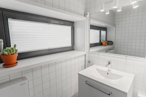 A modern bathroom with a window, a sink, and a mirror.
