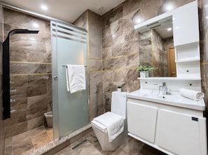 Un baño moderno con ducha de vidrio, un lavabo blanco y un espejo grande sobre el mueble.