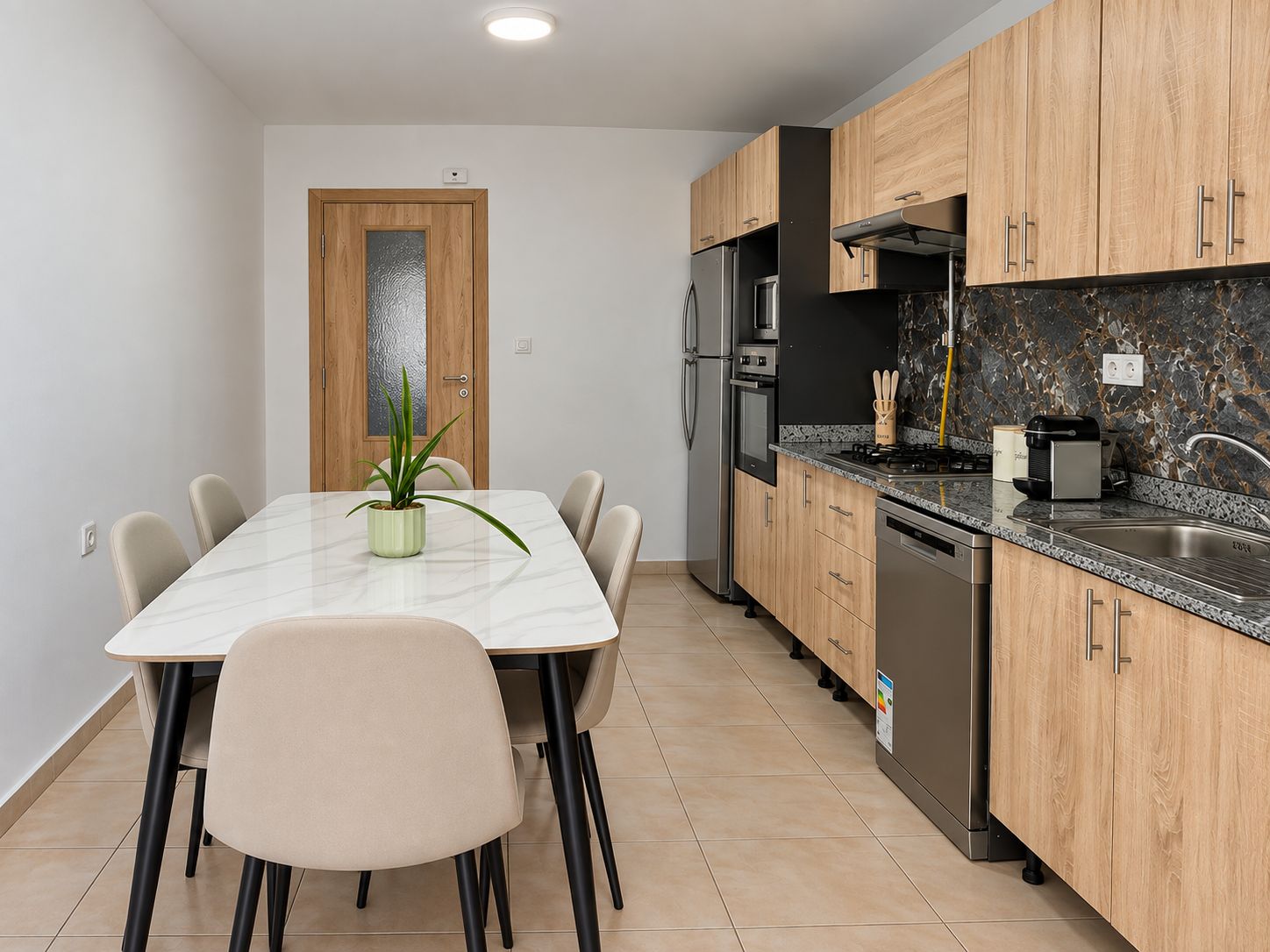 Eine moderne Küche mit Marmorplatte, Holzschränken und einem Essbereich mit einem weißen Tisch und Stühlen.