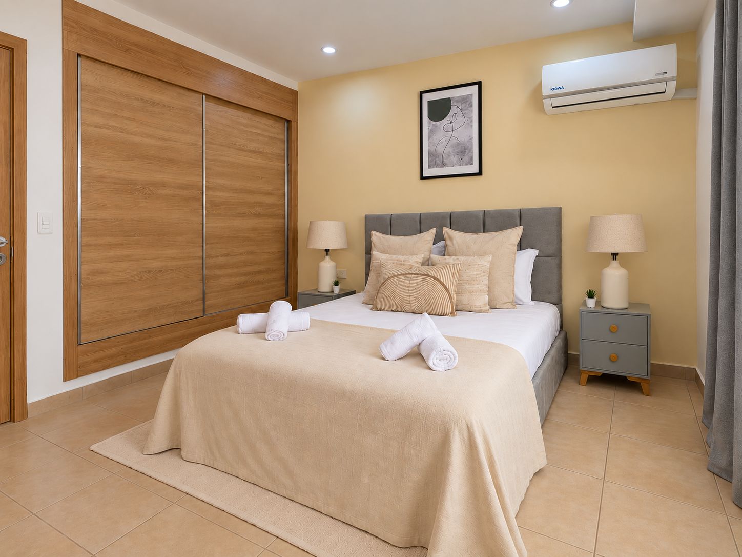 Een slaapkamer met een bed, twee nachtkastjes, een airconditioningapparaat, een ingelijst schilderij aan de muur en een houten garderobekast.