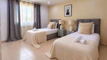 A hotel room with two beds, a large window with curtains, a framed picture on the wall, and a tiled floor.