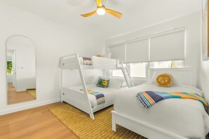 Ein Zimmer mit einem Etagenbett, einem Fenster mit Jalousien, einem Deckenventilator und einer Tür zu einem anderen Raum.