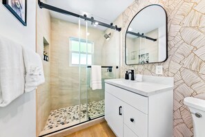 A modern bathroom with a glass-enclosed shower, a white vanity with a black faucet, and a large mirror. - Tourmaline Beach Compound - Two Homes, One Getaway (San Diego)