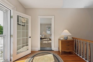 A hallway with a wooden floor, a lamp, a wooden dresser, and a door leading to another room.