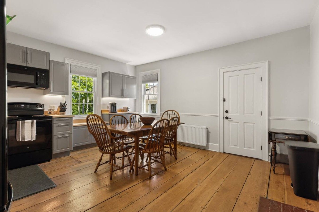 A modern kitchen with a dining area, wooden flooring, and a white door.