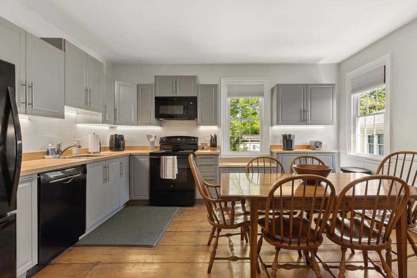 A modern kitchen with grey cabinets, a black microwave, and a wooden dining table with chairs.
