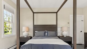 A four-poster bed with a dark headboard, two bedside tables with lamps, and a view of a green landscape through a window. - The Federal Flat Steps From Downtown (Belfast)