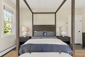 A four-poster bed with a dark headboard, two bedside tables with lamps, and a view of a green landscape through a window. - The Federal Flat Steps From Downtown (Belfast)