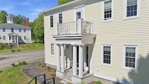 A two-story house with a front porch, a small staircase, and a road in the background. - The Federal Flat Steps From Downtown (Belfast)